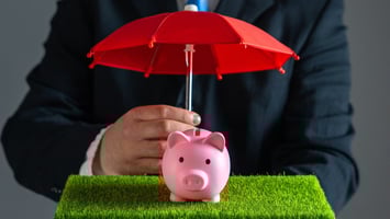 Businessman protects piggy bank with red umbrella.