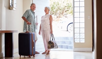 Senior Couple Standing By Front Door With Suitcase About To have a Vacation