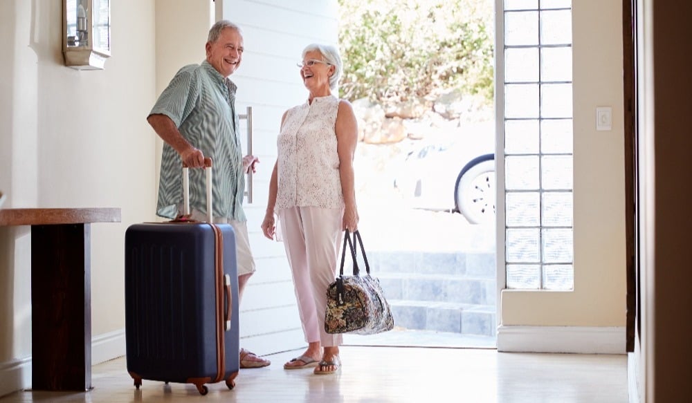 Senior Couple Standing By Front Door With Suitcase About To have a Vacation